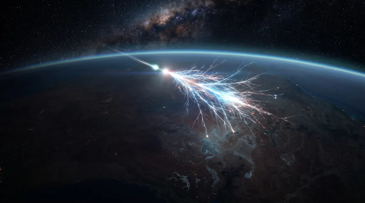 A single glowing particle streaking into Earth's upper atmosphere at night and bursting into a branching cascade of light high above the dark Australian outback.